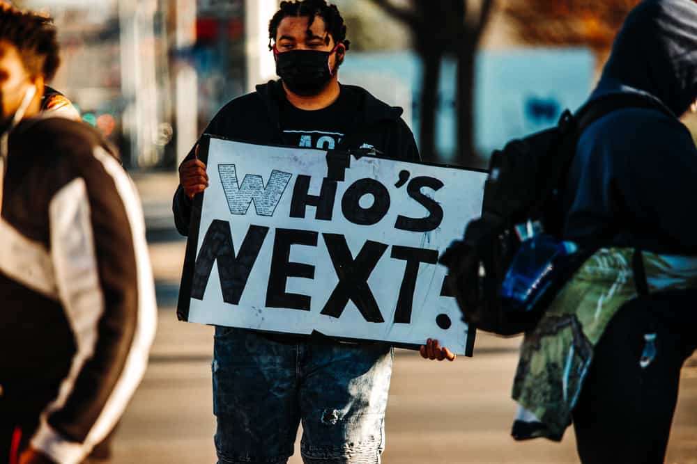 Protestor holding a sign that says "Who's Next"