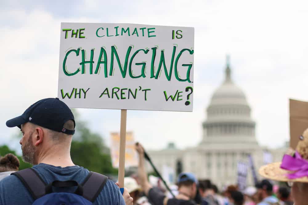 Man holding a sign saying "The Climate is Changing, Why aren't we?"