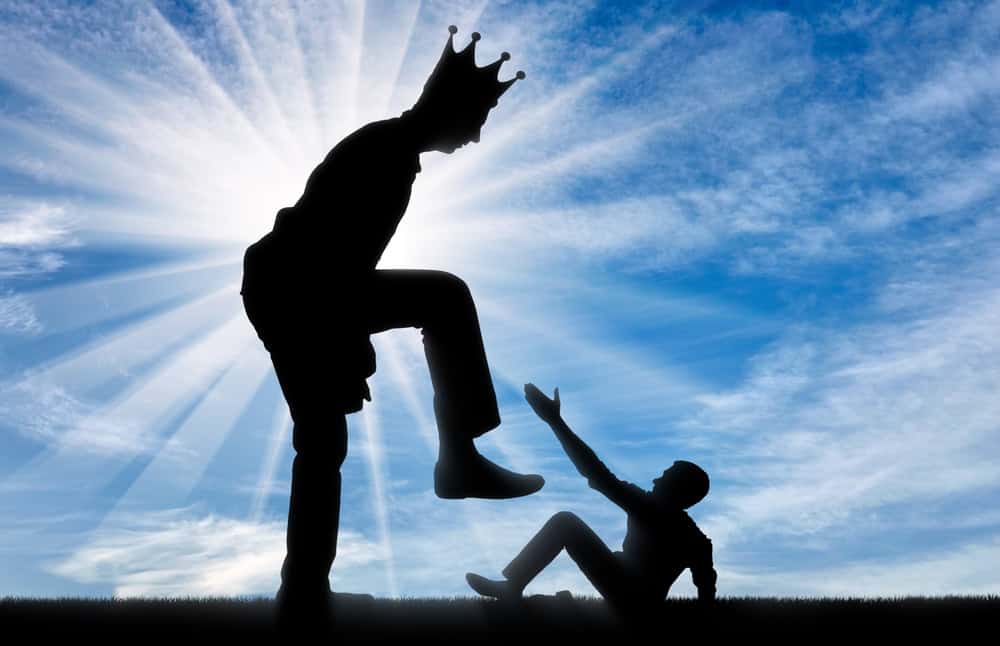 A man with a crown on stomping on a smaller man who is reaching his hand up in desperation