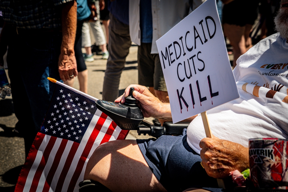Sign saying "Medicaid cuts KILL" and an American flag