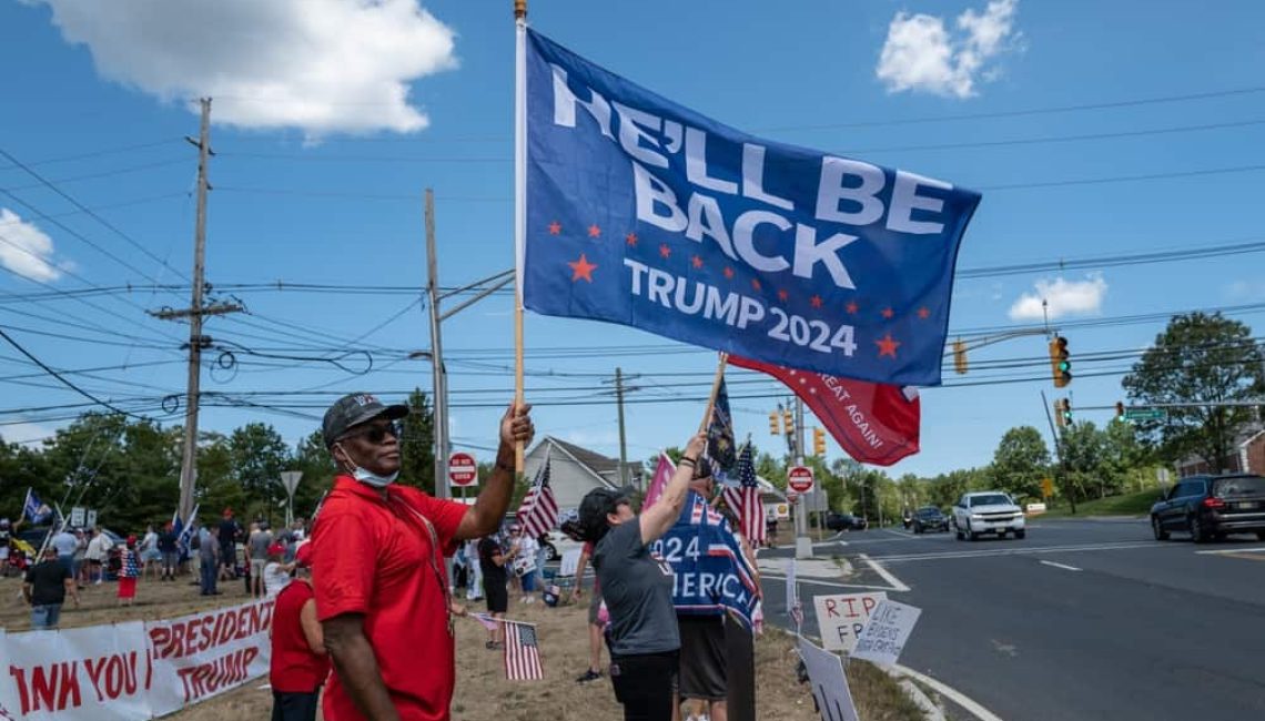 A protester waving a flag that says "He'll be back 2024"