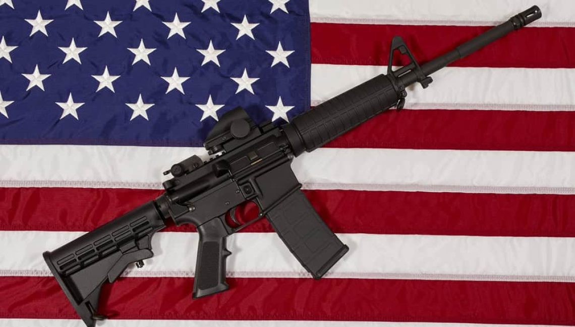 An assault rifle laying on top of the American flag